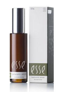 En brun flaske med Hyaluronic Serum med sølvhette står ved siden av en hvit og grå eske, begge merket "Hyaluronic Serum" for ansiktspleie.