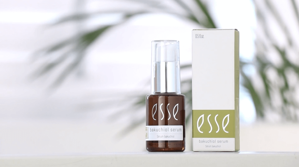 En flaske med Esse Bakuchiol Serum med dråpeteller står ved siden av den matchende esken på en hvit flate, mot en mykt uskarp grønn bakgrunn.