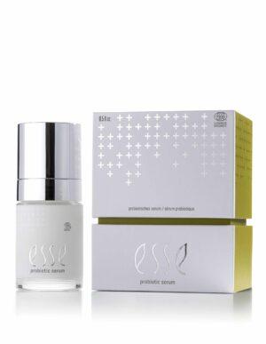 En hvit flaske med Esse Probiotic Serum med sølvglinsende hette vises ved siden av den hvite og gule emballasjen, som har sølvfarget kryssmønster og produktmerkevare.