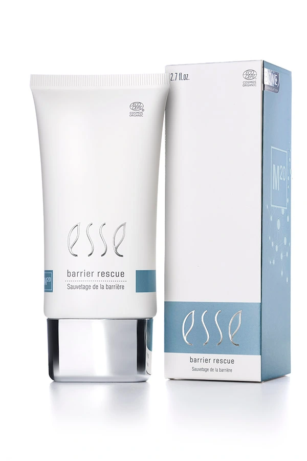 En hvit tube på 2,7 fl oz med påskriften «Esse Barrier Rescue» står ved siden av den tilhørende esken; begge har minimalistiske blå og grå detaljer og fremhever at de er sertifisert økologiske.